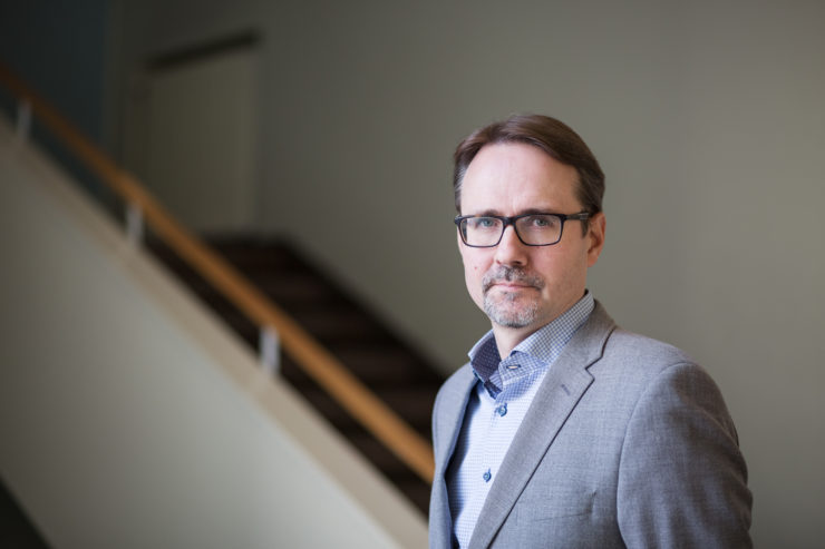 Professor Janne Kivivuori, Helsinki University. He has short, brown hair and glasses. He is wearing a light grey jacket and light blue shirt. In the background there is a staircase.