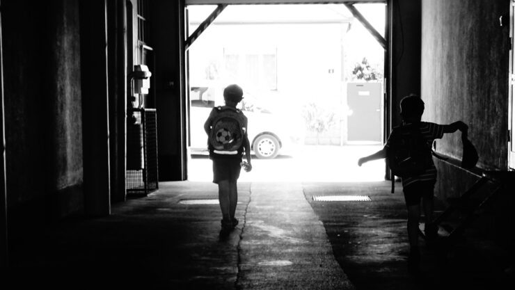 Silhouette of two kids walking through an alley towards a sunny street