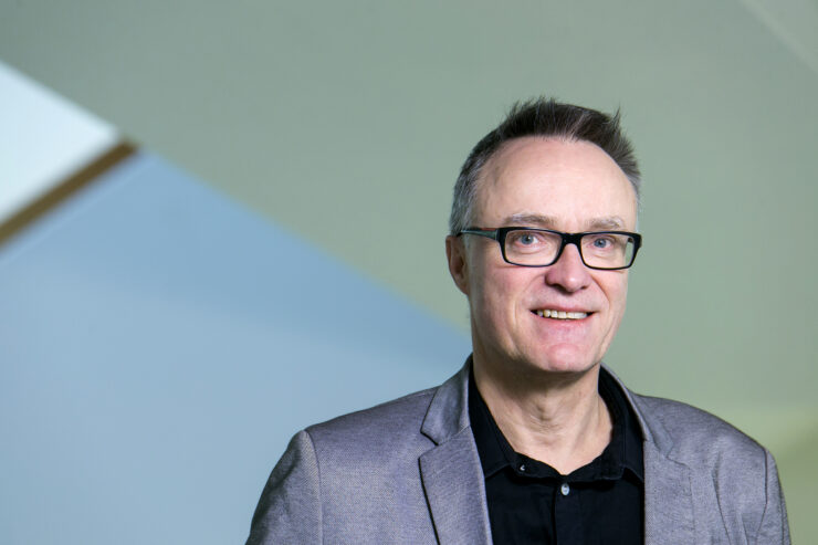 Portrait photo of Helgi Gunnlaugsson, a middle-aged white man with black-rimmed glasses, wearing a grey suit jacket and black shirt.