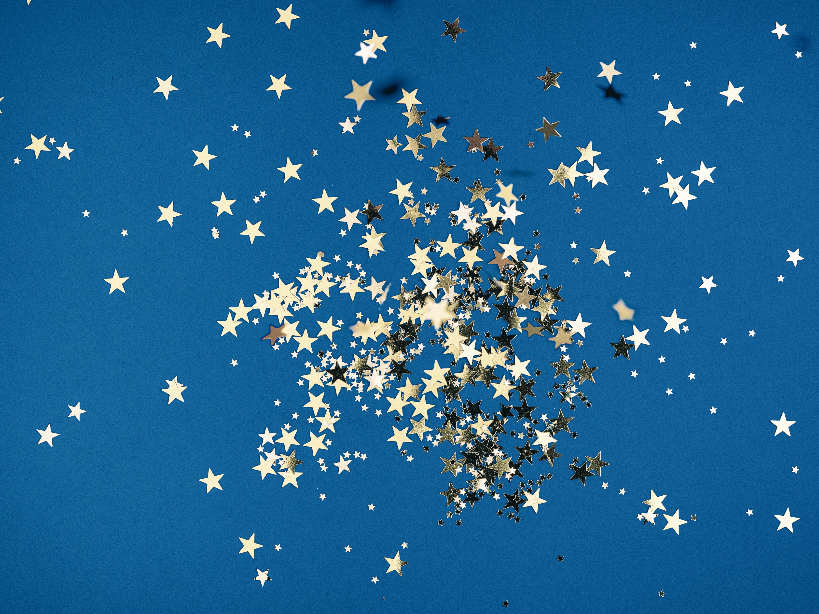 Gold star-shaped confetti on a blue background. Photo by Kier in Sight Archives on Unsplash